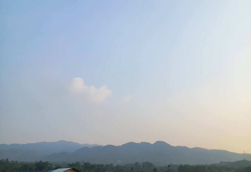 Sawah hijau di Desa Pematang dengan gubuk petani dan pegunungan di latar belakang, lokasi sengketa Batu Batas 100 tahun