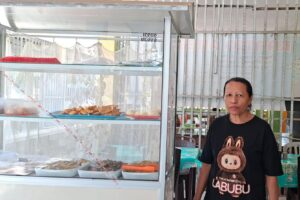 Hana Agsamina Patttypelohi pemilik usaha kantin di Kupang berdiri di depan etalase makanan dengan dukungan KUR BRI